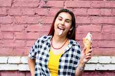 快乐的时尚的女人红色的头发吃冰奶油粉红色的砖墙背景街