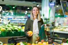 年轻的女人选择选择生态袋蔬菜水果橙子超市