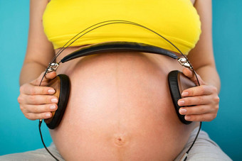 怀孕了女人持有耳机肚子婴儿享受最喜欢的音乐蓝色的背景<strong>孕妇母亲</strong>怀孕爱概念