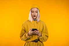 女孩白色头发不寻常的化妆智能手机冲浪互联网黄色的工作室背景现代技术应用程序社会网络