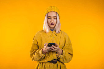女孩白色头发不寻常的化妆智能手机冲浪互联网黄色的工作室背景现代技术应用程序社会网络