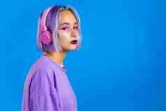 漂亮的女孩染色紫罗兰色的头发听音乐微笑跳舞耳机工作室蓝色的背景音乐跳舞广播概念