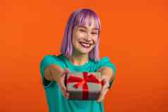 兴奋女人紫罗兰色的头发持有礼物盒子手相机橙色墙背景女孩微笑快乐现在工作室肖像
