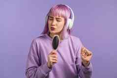 年轻的漂亮的女人紫罗兰色的发型唱歌跳舞头发刷梳子麦克风紫罗兰色的墙女孩耳机有趣的听音乐梦想名人