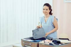 快乐女人小心翼翼地包装色彩斑斓的夏天衣服行李手提箱旅程