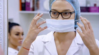 <strong>美容</strong>房间诊所女医生穿眼镜穿白色统一的礼服医疗帽绷带站前面镜子