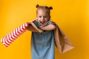 肖像高加索人美丽的快<strong>乐学</strong>前教育女孩微笑快乐的持有重纸板袋孤立的橙色黄色的背景幸福消费主义出售人购物概念