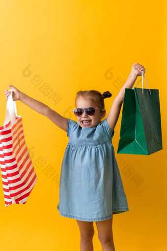肖像美丽的快<strong>乐学</strong>前教育女孩太阳镜微笑快乐的持有电梯纸板袋孤立的橙色黄色的背景幸福消费主义出售人购物概念