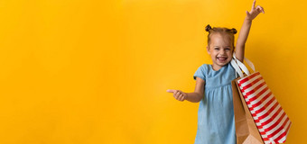 横幅肖像美丽的快<strong>乐学</strong>前教育女孩微笑快乐的持有纸板袋点手指一边橙色黄色的背景幸福消费主义出售人购物概念