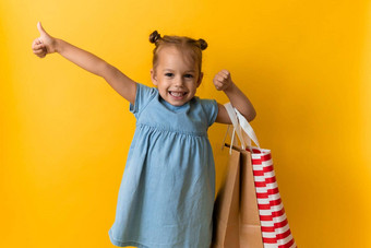 肖像高加索人美丽的快<strong>乐学</strong>前教育女孩微笑快乐的持有纸板袋拇指孤立的橙色黄色的背景幸福消费主义出售人购物概念