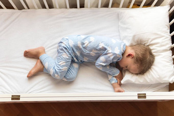 前视图可爱的年学前教育婴儿男孩孩子睡觉甜美白色婴儿床午餐休息时间蓝色的睡衣枕头首页童年休闲安慰医学健康概念