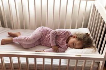前视图可爱的年学前教育婴儿女孩孩子睡觉甜美白色婴儿床午餐休息时间粉红色的睡衣枕头首页童年休闲安慰医学健康概念