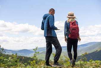 后视图徒步旅行夫妇背包站山前享受美丽的景观男人。女人在户外徒步旅行站岩石