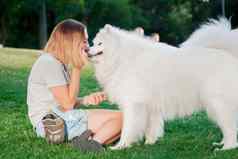 成人女人红色的头发戏剧中风狗萨莫耶德人品种白色毛茸茸的宠物公园情妇绿色草坪上有趣的