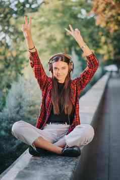 年轻的少年听音乐耳机公园女孩红色的格子衬衫微笑跳舞节奏概念学生生活自由现代青年