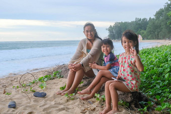快乐亚洲家庭妈妈。女儿坐着日志微笑相机海滩夏天假期日落夏天家庭旅行海滩旅行假期概念
