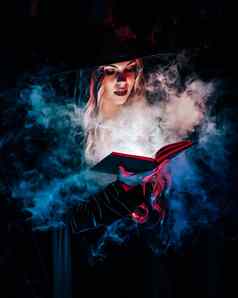 美丽的女巫阅读魔法书黑暗背景森林万圣节金发女郎向导服装概念漂亮的女人蓝色的烟