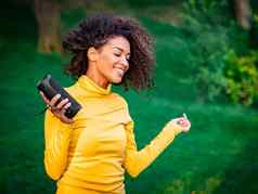 现代时尚的非洲美国女孩听音乐无线可移植的演讲者年轻的美丽的女人享受跳舞公园