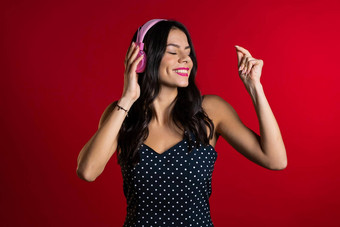 漂亮的年轻的女孩长头发有趣的微笑跳舞粉红色的耳机工作室红色的背景音乐跳舞广播概念