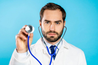 肖像年轻的英俊的男人。专业医疗白色外套听诊器孤立的蓝色的工作室背景男人。点仪器相机听生病了病人