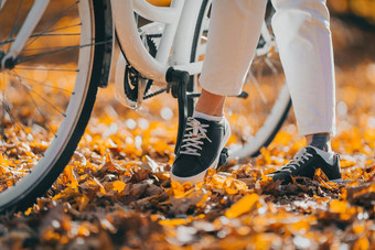 特写镜头腿女人白色裤子骑自行车秋天公园阳光明媚的一天金叶子秋天黄色的森林认不出来女孩古董自行车健康的生活方式审美图片
