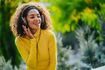 特写镜头非洲美国女人听音乐耳机在户外年轻的女孩卷曲的发型黄色的享受音乐公园