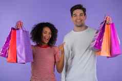 跨种族购物狂夫妇持有购物纸袋紫色的工作室背景白色男人。非洲女人买了礼物销售折扣中心检疫