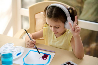 高加索人女孩穿无线耳机听音乐绘画画图片纸