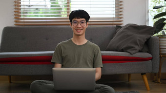年轻的亚洲男人。坐着生活房间学习在线虚拟教室移动PC教育电子学习距离培训