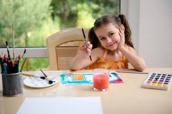 快乐的女孩坐着表格精明地微笑相机绘画水彩画画笔