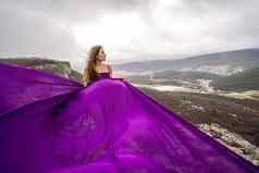 女人长头发站紫色的流动衣服流动织物山背景天空云