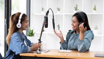 微笑亚洲年轻的女人男人。广播主机耳机麦克风说话谈话记录播客广播工作室技术使记录音频概念