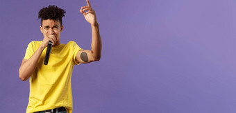 肖像年轻的无忧无虑的时髦的赶时髦的人的家伙纹身黄色的t恤执行前面观众嘻哈说唱唱歌首歌提高手指持有麦克风<strong>卡拉ok</strong>