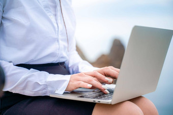 女人坐着打字<strong>苹果笔记本</strong>电脑键盘阳台美丽的海视图穿白色上衣黑色的裙子自由旅行假期概念数字游牧