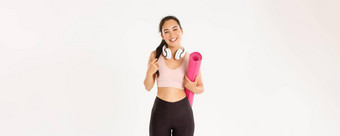 体育运动幸福活跃的生活方式概念微笑快乐亚洲健身女孩耳机运动服装携带橡胶席锻炼瑜伽笑无忧无虑的白色背景