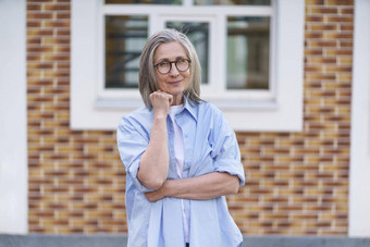 成熟的灰色头发女人穿眼镜站户外旅行世界退休高级女人会议家庭成熟的女人完美的皮肤穿蓝色的衬衫站