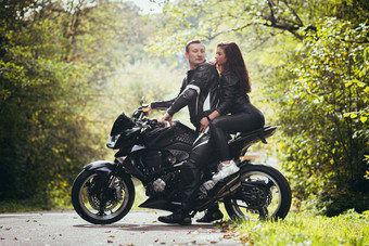 英俊的年轻的男人。美丽的年轻的女孩夫妇坐着摩托车站摩托车黑色的皮革衣服拥抱自然街