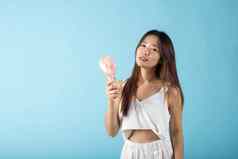 亚洲美年轻的女人持有粉红色的可移植的电迷你风扇脸