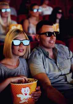 夫妇看电影电影眼镜吃爆米花零食年轻的男人。女人坐着看行动电影电影娱乐日期剧院