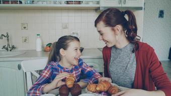 快乐的妈妈。可爱的女儿早餐吃松饼羊角面包会说话的首页现代厨房家庭食物首页人概念
