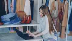 有吸引力的年轻的女商人坐着会说话的移动电话工作移动PC服装商店时尚的服装鞋子袋背景