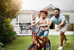 学习自行车骄傲爸爸教学年轻的儿子骑穿头盔安全家庭首页花园活跃的父亲帮助支持孩子骑自行车