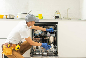 修理工统一的维修洗碗机厨房年轻的男人。专家擅抖着部分螺丝刀检查状态托盘菜一边视图