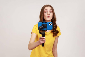 年轻的有吸引力的女人相机电话稳定剂芽视频视频博客使接吻手势穿黄色的休闲风格t恤
