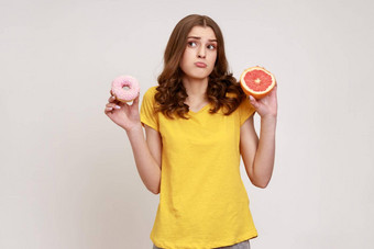 健康的水果高热量的甜点肖像困惑卷发青少年女孩休闲风格t恤选择葡萄柚甜甜圈