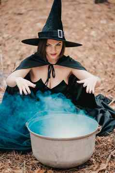 黑色的女巫坐在前面大锅烟下降女巫召唤啤酒药水法术恐怖万圣节动漫真人秀假期魔法概念
