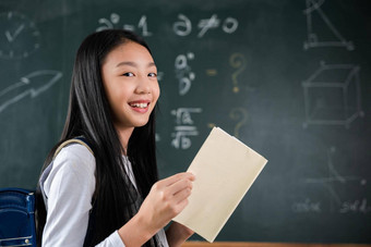 快乐美丽的亚洲女学生女孩站持有书站前面黑板上教室