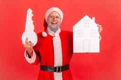微笑上了年纪的男人。灰色的胡子穿圣诞老人老人服装持有手纸房子关键快乐买公寓