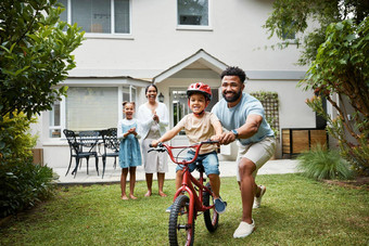 男孩自行车学习骄傲爸爸快乐家庭首页花园在户外微笑父亲教学有趣的技能帮助支持兴奋年轻的儿子骑周期踏板自行车