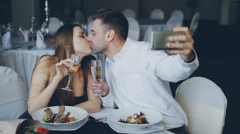 有吸引力的爱的夫妇采取自拍香槟眼镜智能手机晚餐餐厅微笑接吻摆姿势相机